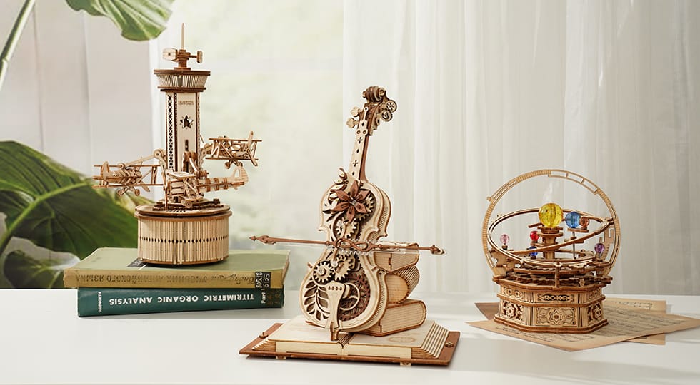 Three intricate wooden 3D puzzles: an airplane carousel, a cello, and an orrery.
