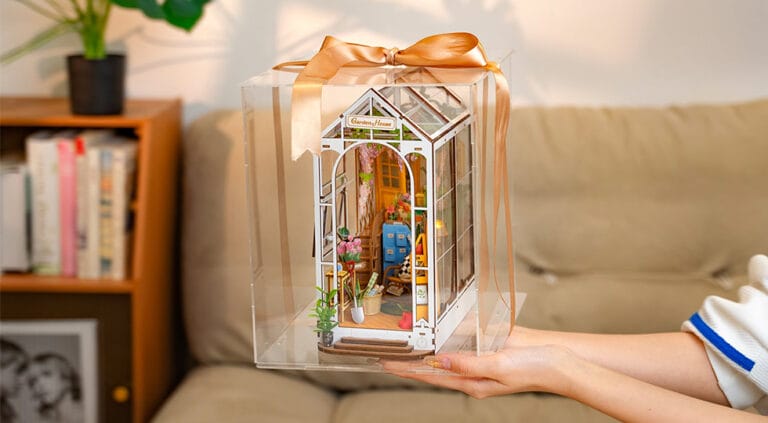 Miniature wooden greenhouse displayed in a clear acrylic box, tied with a ribbon.