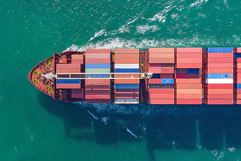 Aerial view of a large container ship at sea, carrying numerous cargo containers.
